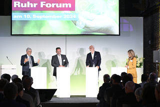 Das Bild zeigt eine Diskussionsrunde auf dem Ruhr Forum mit mehreren Rednern an Podien. Im Hintergrund ist eine Präsentation zu sehen.